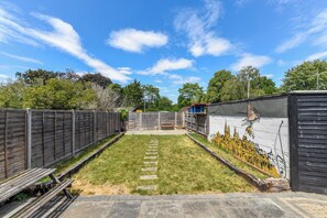 A backyard with a paved patio, a wooden fence, and a mural on the wall. - Florence of Oxford (Oxford)