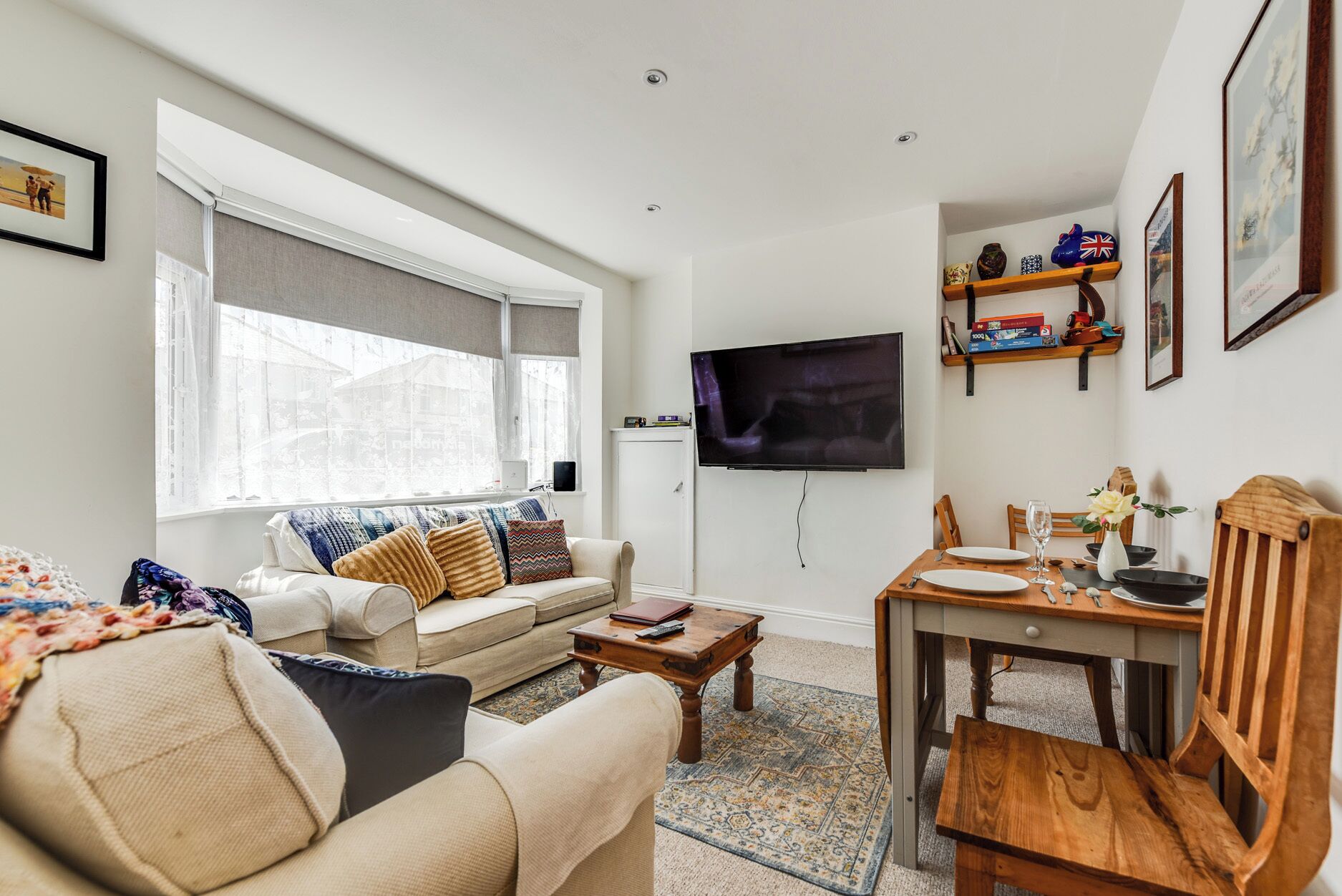 Un salon comprenant un canapé, une table basse, un téléviseur fixé au mur, une table à manger avec des chaises et une fenêtre avec des rideaux.