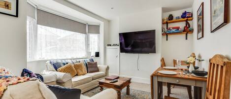 Un salon comprenant un canapé, une table basse, un téléviseur fixé au mur, une table à manger avec des chaises et une fenêtre avec des rideaux.