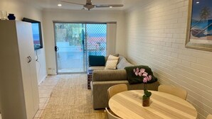 Une pièce comprenant un canapé, une table à manger avec des chaises, une petite plante en pot et une porte-fenêtre coulissante donnant sur un espace extérieur.