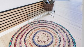 Una habitación con un banco de madera, una alfombra colorida, un espejo y vistas a un espacio exterior con una mesa y sillas.