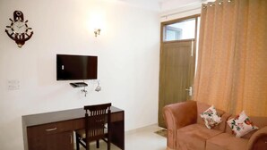 A room with a desk, chair, sofa, television, and a door with curtains. - Fortune Home Service Apartment E-28 2B (New Delhi)