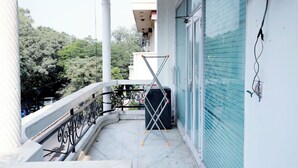 A balcony with a metal railing, a black object on the floor, and a view of trees and buildings. - Fortune Home Service Apartment E-28 2B (New Delhi)