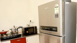 A kitchen with a stainless steel refrigerator, a gas stove, a microwave, and red cabinets. - Fortune Home Service Apartment E-28 2B (New Delhi)