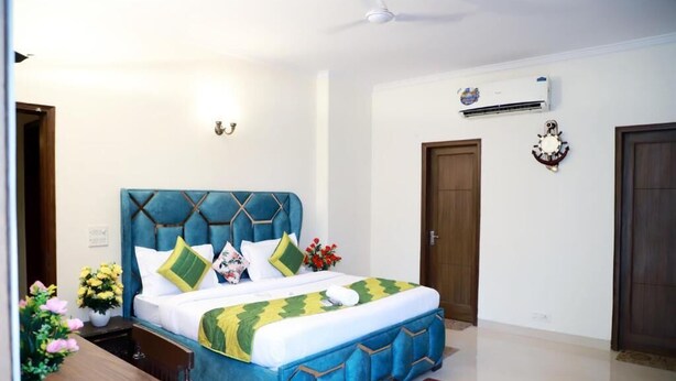 A bedroom with a bed, bedside tables, a nightstand, an air conditioning unit, and a wall clock. - Fortune Home Service Apartment E-28 2B (New Delhi)