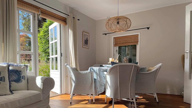 Ein Zimmer mit einem weißen Sofa, Korbstühlen, einem Esstisch und einer hängenden Weidenleuchte.