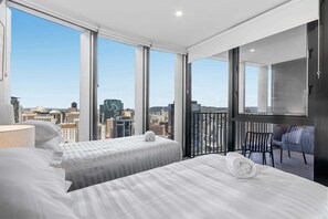 Ein Hotelzimmer mit zwei Betten, einem Balkon mit einem Stuhl und Blick auf die Stadt.