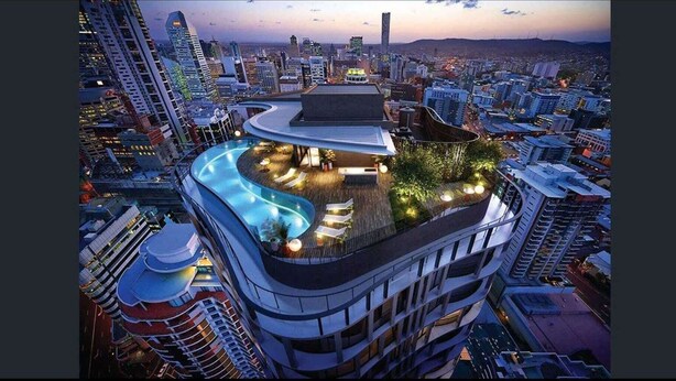 A high-rise building with a rooftop pool and lounge area, surrounded by other buildings. - Luxury Sky-high CBD Apt | Pool, Gym, Parking (Brisbane City)