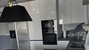 A modern kitchen with stainless steel appliances, a black countertop, and a wooden shelf with greenery.