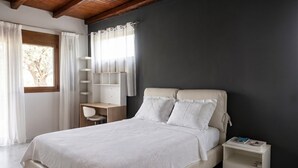 A bedroom with a bed, a nightstand, a desk, and a window with curtains.