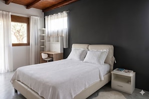 A bedroom with a bed, a nightstand, a desk, and a window with curtains.