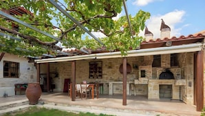 A stone building with a covered patio, a large terracotta pot, and a brick oven.