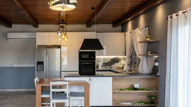 A modern kitchen with a dining area, wooden ceiling beams, and built-in appliances.
