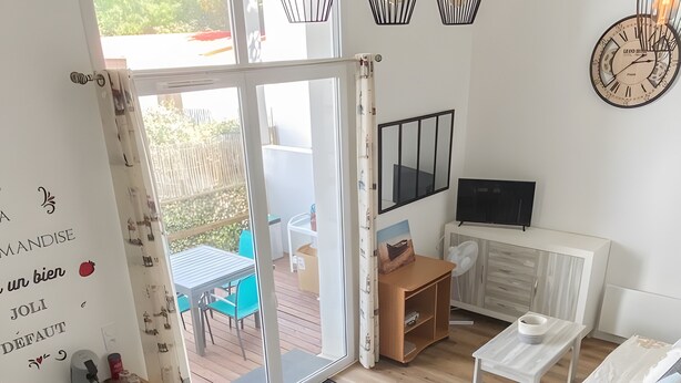 A modern living room with a dining table, chairs, a sofa, a TV, and a balcony with a table and chairs. - The Geraniums Apartment - ref 305 (La Tranche-sur-Mer)