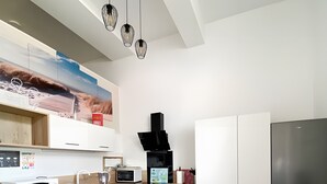 A modern kitchen with white cabinets, a stainless steel refrigerator, and a dining table with blue chairs. - The Geraniums Apartment - ref 305 (La Tranche-sur-Mer)