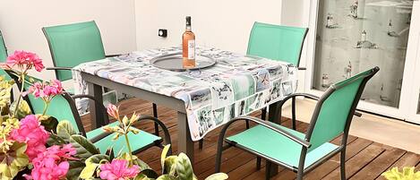 A table with a patterned tablecloth, four chairs, a bottle, and potted plants.