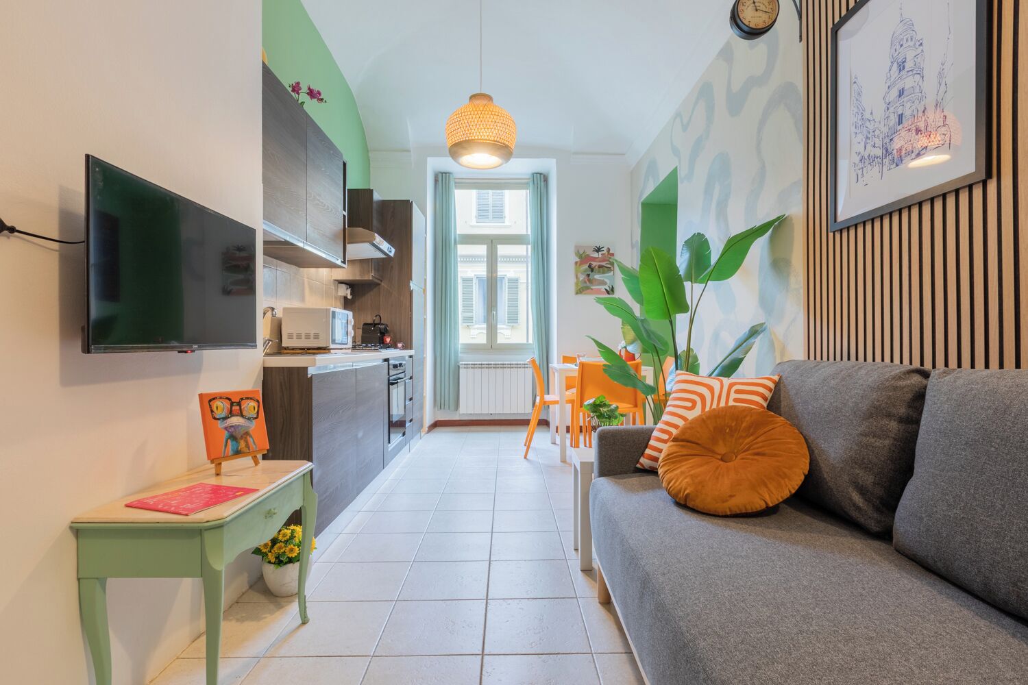 Ein modernes Wohnzimmer mit einem grauen Sofa, einem kleinen Tisch mit Pflanze und einem an der Wand befestigten Fernseher.