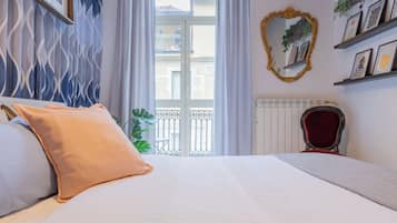 Une chambre d’hôtel avec un lit, un radiateur, une fenêtre avec des rideaux, un balcon et un mur orné de tableaux.