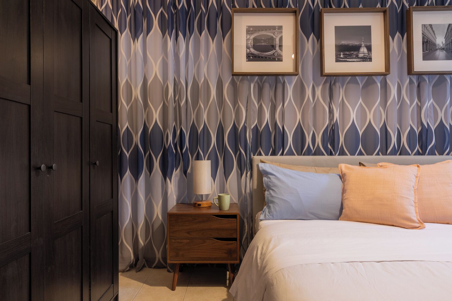 Une chambre à coucher avec un lit, une table de chevet, une lampe et des tableaux encadrés accrochés au mur.