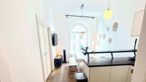 A modern kitchen with white cabinetry, a wooden floor, and a dining area with a bench. - Central Apartment for up to 10 Guests (Hamburg)