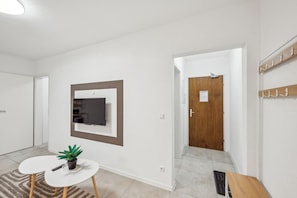 Un interior moderno con un televisor de pantalla plana en la pared, una mesita con una planta, una puerta de madera y un perchero.