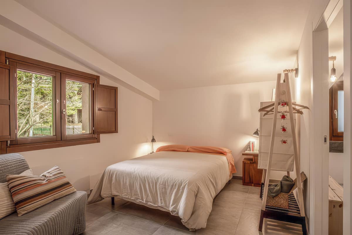 A bedroom with a bed, a chair, a desk, a ladder, and a window.