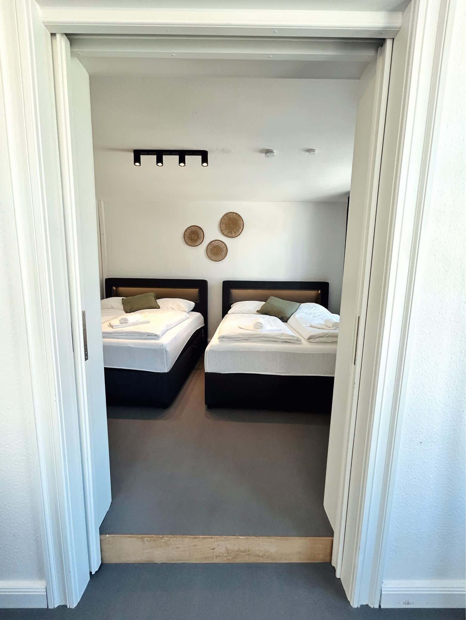 A narrow hallway leading to a room with two beds, a ceiling light, and three wall-mounted circular decorations.