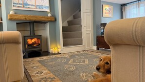 A cozy living room with a fireplace, a dog, and a staircase. - York Cottage (Reydon)