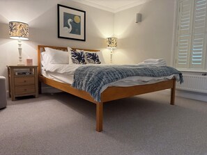 A bedroom with a wooden bed, two bedside tables with lamps, a framed picture on the wall, and a radiator near the window. - York Cottage (Reydon)