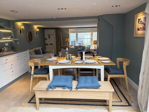 A dining area with a wooden table set for four, a bench, and a view of the garden through a window. - York Cottage (Reydon)