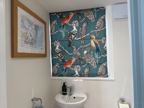 A bathroom with a map, a sink, and a window with a bird pattern. - York Cottage (Reydon)