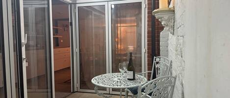 A corner patio with a table and chairs, a candle, and a bottle of wine.