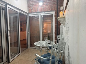 A corner patio with a table and chairs, a candle, and a bottle of wine. - York Cottage (Reydon)