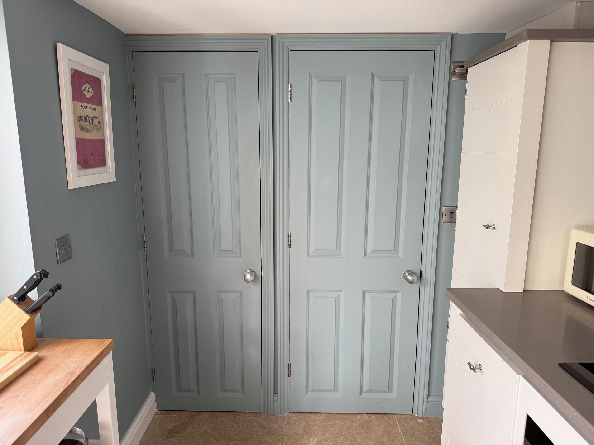 A kitchen with two light blue doors, a wooden countertop, a microwave, and a framed picture on the wall.