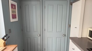 A kitchen with two light blue doors, a wooden countertop, a microwave, and a framed picture on the wall. - York Cottage (Reydon)