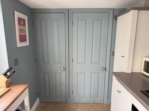 A kitchen with two light blue doors, a wooden countertop, a microwave, and a framed picture on the wall. - York Cottage (Reydon)
