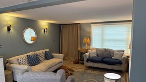 A living room with two sofas, a coffee table, a lamp, a mirror, and a dog. - York Cottage (Reydon)