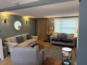 A living room with two sofas, a coffee table, a lamp, a mirror, and a dog. - York Cottage (Reydon)