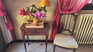 Une chaise en bois avec un siège rembourré, une petite table en bois ornée d’un vase de fleurs, une lampe et un radiateur à l’arrière-plan.