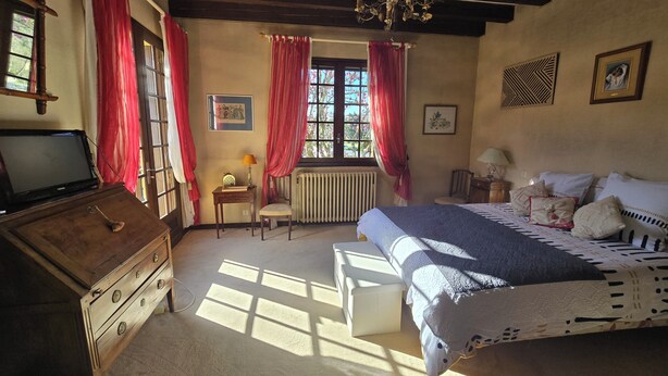 Une chambre à coucher comprenant un lit, une commode, une chaise, une fenêtre avec des rideaux, un radiateur et un lustre.