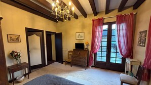 Une pièce comprenant un lit, une commode en bois, une chaise, un bureau, un lustre et une fenêtre avec des rideaux.