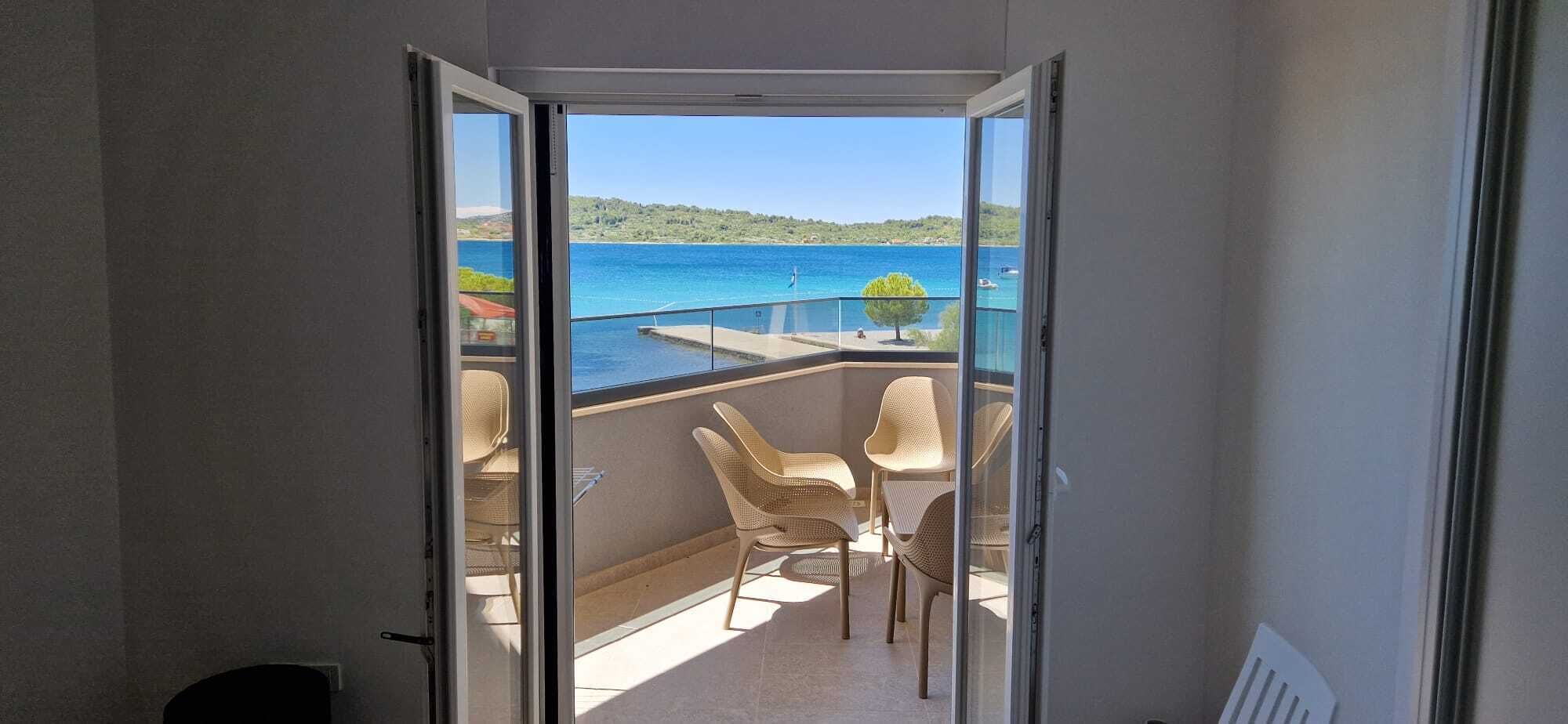A balcony with a view of a body of water, a table, and two chairs.