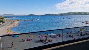 A beach with people sunbathing and swimming, boats in the water, and a view of hills in the distance. - Mare Anima Apartments (Srima)