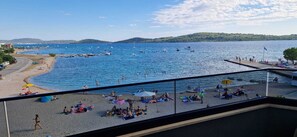 A beach with people sunbathing and swimming, boats in the water, and a view of hills in the distance. - Mare Anima Apartments (Srima)