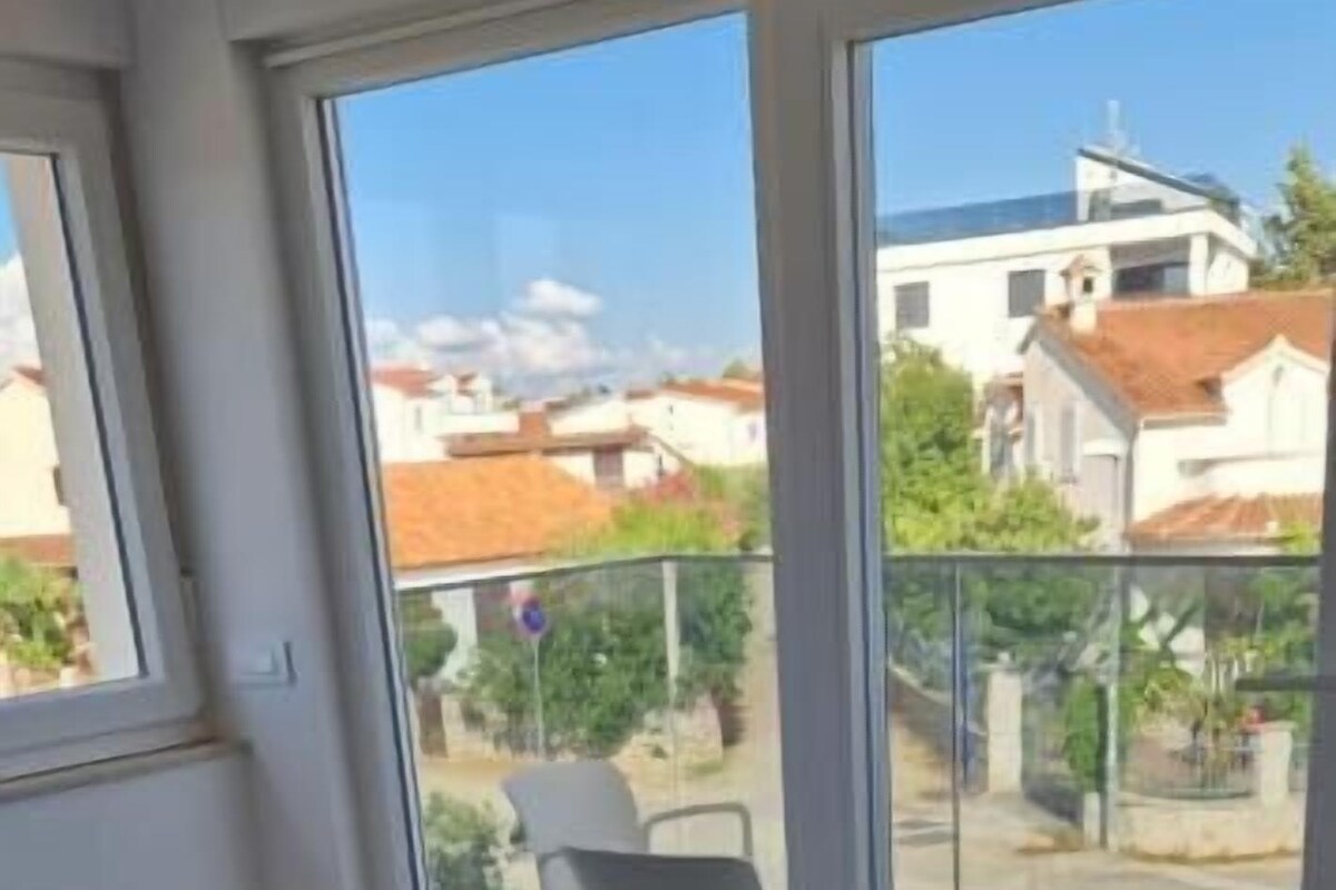 A bedroom with a bed, a balcony with a chair, and a view of buildings.