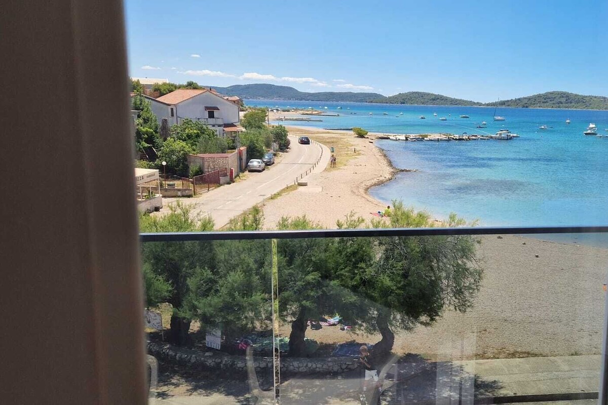 A coastal view from a balcony with a clear beach, boats, and a distant mountain range.