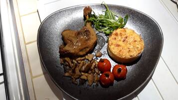 A plate with a grilled chicken leg, mushrooms, cherry tomatoes, and a slice of bread.