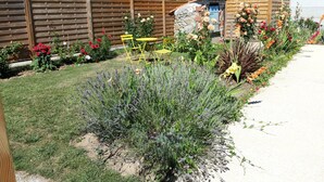 Un jardin avec une clôture en bois, un petit bâtiment en pierre et des chaises pliantes jaunes.