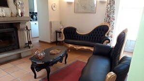 Un salon avec une cheminée, un canapé en cuir noir, un fauteuil assorti, une petite table agrémentée d’objets décoratifs et un tapis rouge.