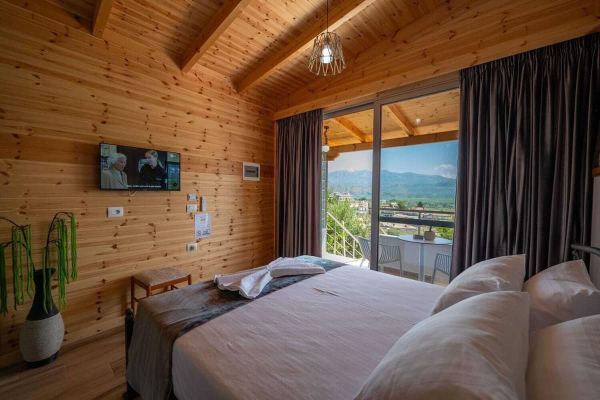 Habitación de cabaña de madera con cama, televisión, ventana con cortinas y vistas al exterior.
